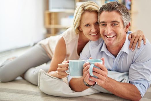 We couldnt be anymore happier. Portrait of a smiling mature couple lying on their living room floor drinking coffee.