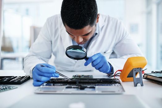 Leave no chip unturned. Shot of a young man using tweezers and a magnifying glass while repairing computer hardware in a laboratory.