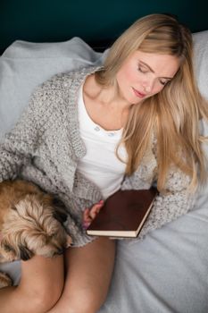 A young woman fell asleep while reading a book. Multi-breed dog.