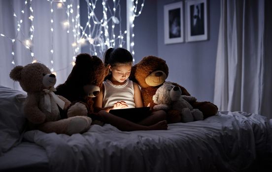 Introducing her teddies to technology. Shot of an adorable little girl using a digital tablet in bed at night.