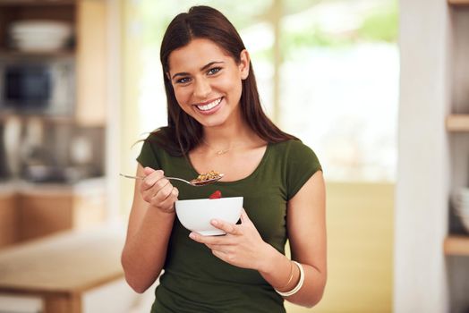 Health is happiness. Portrait of a happy young woman eating a bowl of muesli while standing in her kitchen.