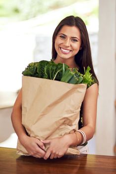 Eating well and feeling great. Portrait of an happy young woman holding a bag of groceries in her kitchen.