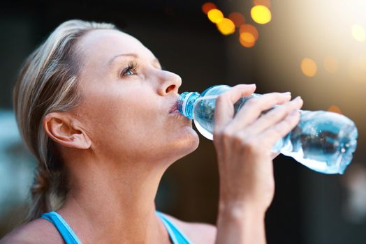 Nothing tastes better than water after an intense workout. Shot of a mature woman drinking water out of a bottle outdoors.