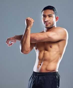 Focused on staying full toned. Studio shot of a muscular young man stretching his arms against a grey background.
