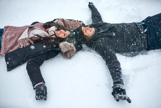 The snow make us feel like kids again. High angle shot of a couple lying in the snow making snow angels.