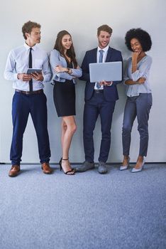 Keeping up with business in the online space. Shot of a diverse group of businesspeople using wireless technology while standing against a grey background.