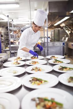 Capable hands in the kitchen. Shot of a chef plating food for a meal service in a professional kitchen.