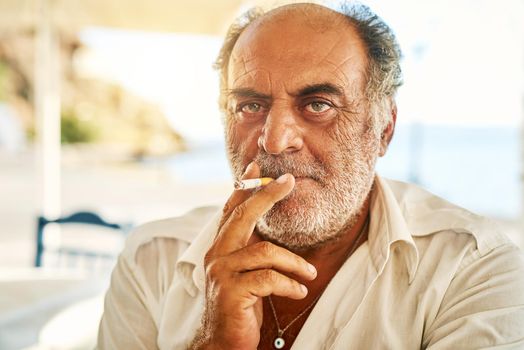 He is one tough guy. Portrait of a confident senior man smoking a cigarette and standing outside while looking at the camera.