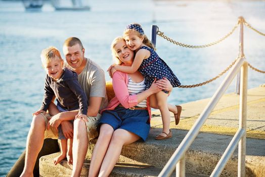 Portrait of a family with young children posing together by the harbor.