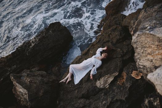Beautiful bride in long white dress wet hair lying on a rocky cliff unaltered