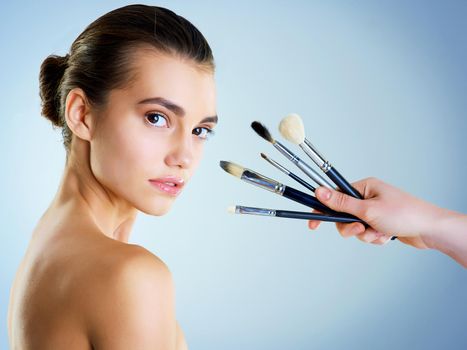 Makeup is an expression of me. Studio portrait of a hand holding makeup brushes next to a beautiful young woman against a blue background.