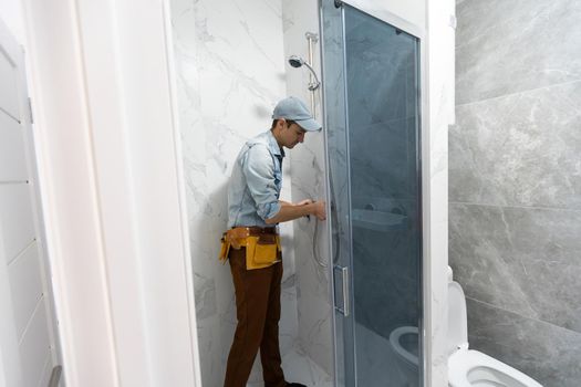 Workers are installing glass door of the shower enclosure.