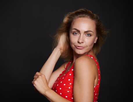 Beautiful middle aged blonde sporty European woman in red swimsuit with white polka dots confidently looking at camera isolated over black background with copy ad space