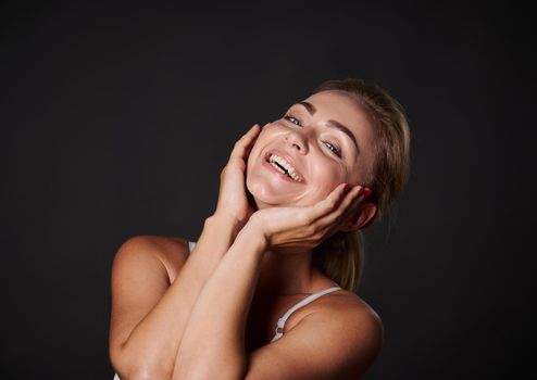 Attractive Caucasian middle aged woman with fresh glowing skin smiles with beautiful toothy smile, isolated over black background. Anti-aging concept, smoothing, rejuvenating beauty treatment