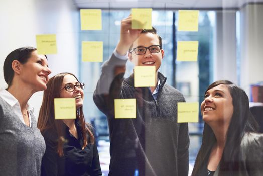 We should put our ideas together. Cropped shot of a group of businesspeople brainstorming on a glass wall in an office.