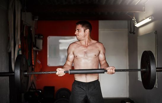 Increasing his strength. Cropped shot of a handsome and muscular young man working out with a barbell in the gym.