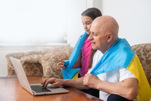Grandfather and granddaughter with laptop and flag of Ukraine