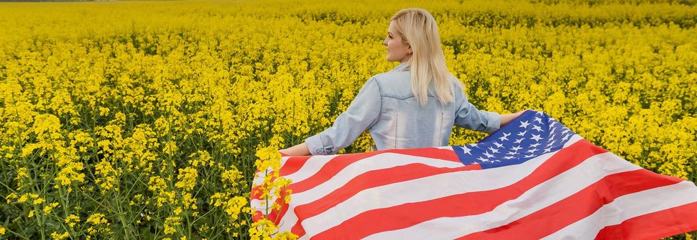 Adult woman holding American flag with pole, stars and stripe in a yellow rapeseed field. USA flag fluttering in the wind