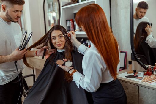 Professional makeup artist and hairstylist preparing female customer in beauty salon. Beauty salon