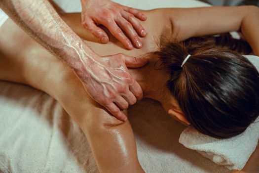 Hands of masseur man doing back massage with oil to a woman in spa salon. Therapy, resort