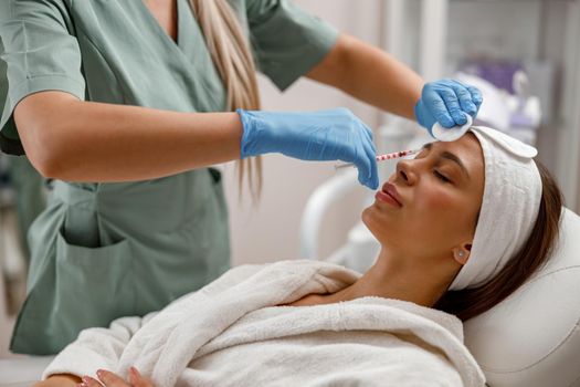 Professional beautician making injections, filling female face with hyaluronic acid