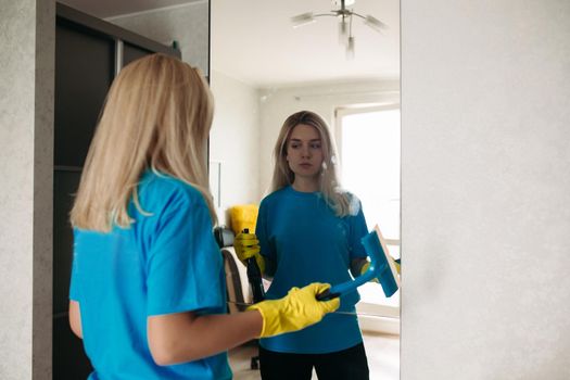 Female employee of cleaning company washing mirror.