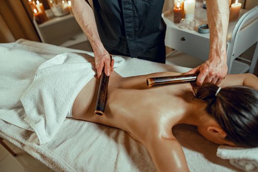 Male therapist hands doing back massage to female client with hollow bamboo canes