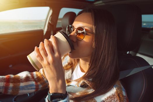 Young beautiful woman driving a car and drinking coffee.