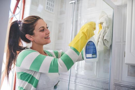 Getting rid of grease and grime. Shot of a young woman cleaning a bathroom shower door.