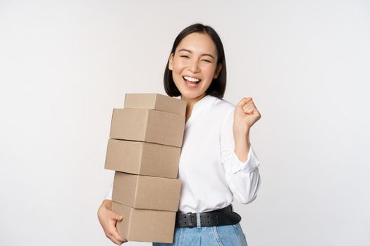 Enthusiastic korean girl shopper, holding boxes delivery and smiling happy, standing over white background
