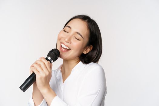 Close up portrait of asian woman singing in microphone at karaoke, standing over white background