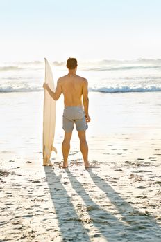 Ive never seen a more beautiful view. Rearview shot of a muscular young man holdng his surfboard while on the beach.