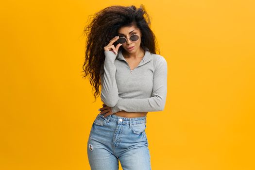 COOL OFFER. Sexy pretty millennial Latin female with afro in sunglasses and casual clothes, stay isolated over yellow background. Copy space, free place, fashion banner