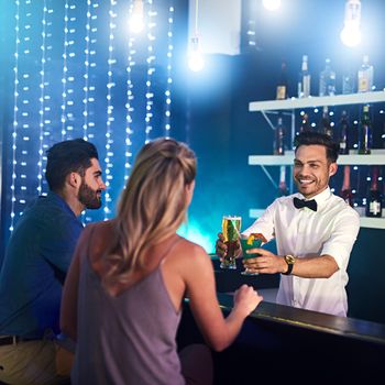 His skill and personality keep his customers satisfied. Shot of a happy bartender serving drinks to a couple in a nightclub.
