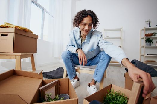 guy with curly hair unpacking things from boxes in the room Lifestyle. High quality photo