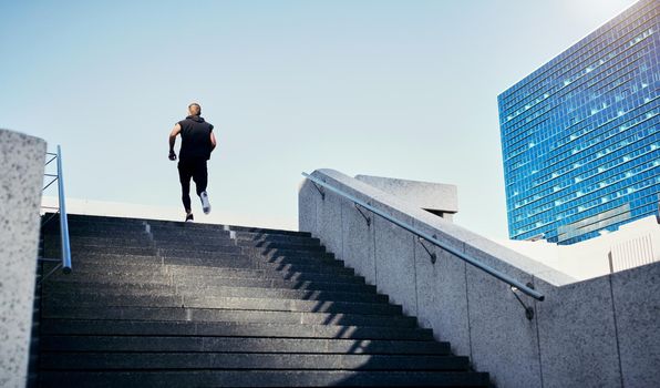 Every step is one step closer to your goal. Rearview shot of a young man running up stairs in the city.