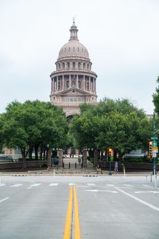 Photo of Texas State Capitol with blue sky and clouds. With green trees in the front of the Capitol building on Congress Avenue