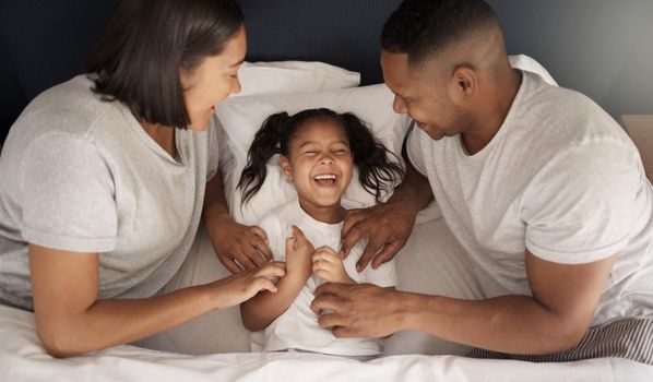 We know your weak spot. Shot of a young couple sitting in bed and bonding with their daughter by tickling her.