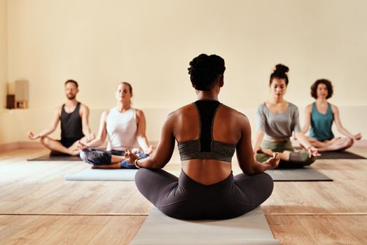 When you believe, you will receive. Shot of a group of young men and women meditating in the lotus position during a yoga session.