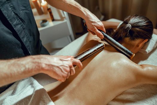 Closeup of male therapist hands doing back massage to woman using hollow bamboo canes