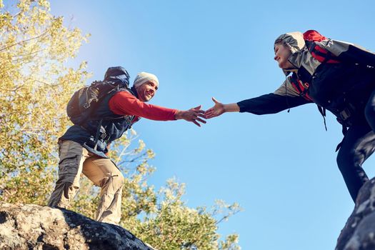 Bridging the divide with teamwork. Shot of a pair of happy hikers reaching for each others hands on a mountain trail.