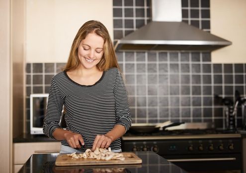 Mushrooms are the secret ingredient. Shot of a happy young woman slicing mushrooms on a chopping board in the kitchen.