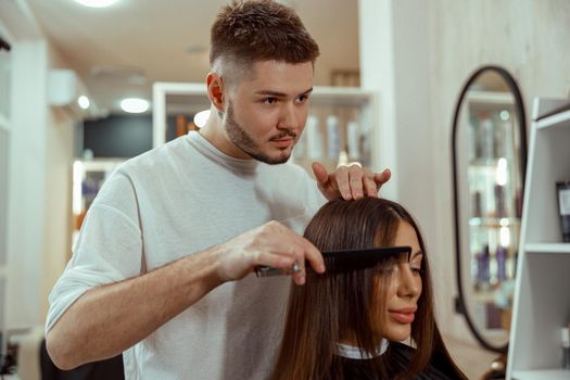 Professional male hairdresser making hairstyle to woman at beauty salon