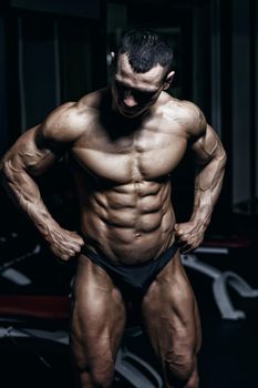 Handsome power athletic bodybuilder training pumping up muscles in gym. Strong bodybuilder with perfect abs, shoulders, biceps, triceps and chest