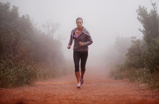 Shes committed to staying in shape. Shot of a woman running on a trail on a misty morning.