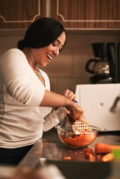 These are going to turn out great. Shot of a cheerful young woman baking cupcakes and grating carrots inside of a kitchen at home.