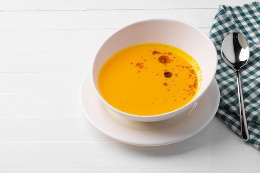Pumpkin creamy soup served in bowl on white wooden background