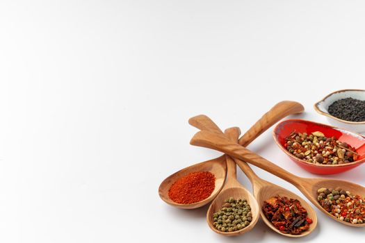 Colorful spices in the wooden spoons on white background.