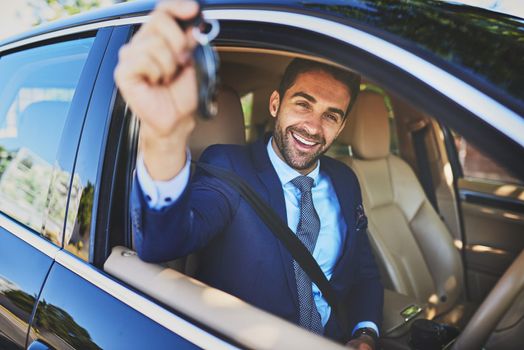 Im on my way to an important meeting. Portrait of a cheerful young businessman holding up keys to the camera while being seated in his car.