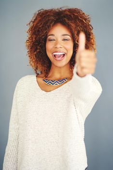 Say yes to happiness. Portrait of a young woman showing thumbs up against a grey background.